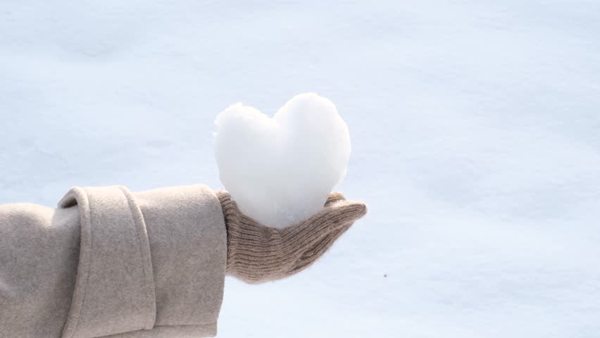Female hand in brown glove holding heart shaped snowball on white background.