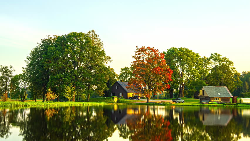 Time lapse of two cabins and trees on a lake, changing seasons from autumn to summer