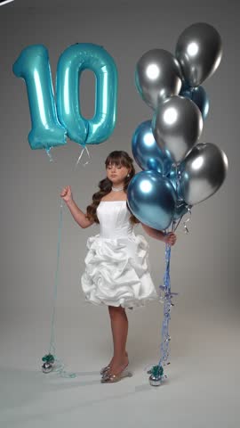 Girl in white dress is holding balloons. Birthday ball concept.