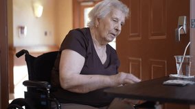 An elderly woman in a wheelchair plays cards at a table in a nursing home. She has a glass of water with a straw nearby.  - Powered by Shutterstock - Get 15% off with code: PIKWIZARD15