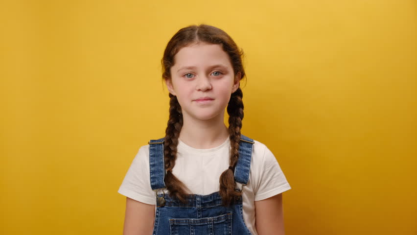 Portrait of charming smiling preteen girl child showing victory v-sign gesture, posing isolated over plain yellow color background wall in studio. Childhood lifestyle concept