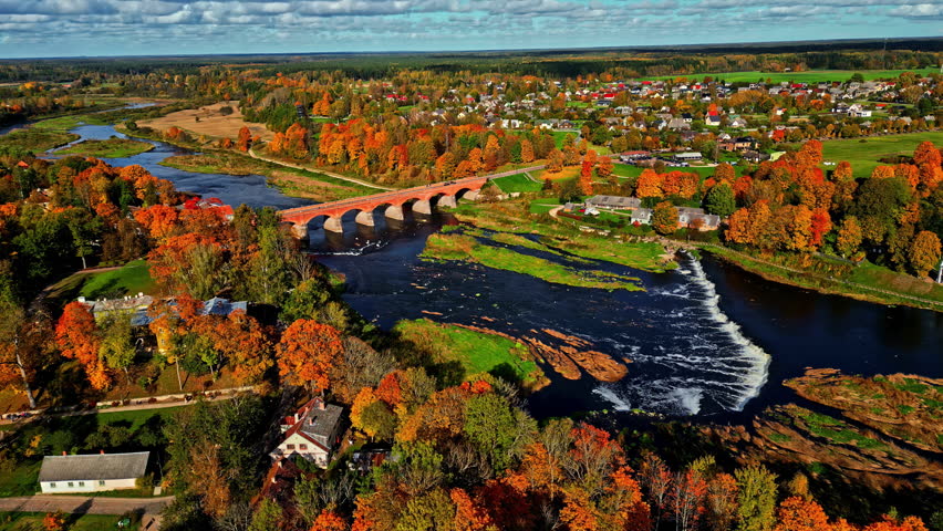 Autumn aerial view of Venta river with iconic rapid waterfall and brick bridge