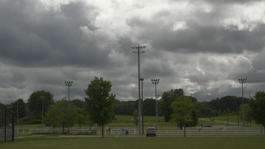 A timelapse of a busy soccer field with people playing while stormy clouds roll overhead, and high winds blow trees in Orillia, Ontario Canada