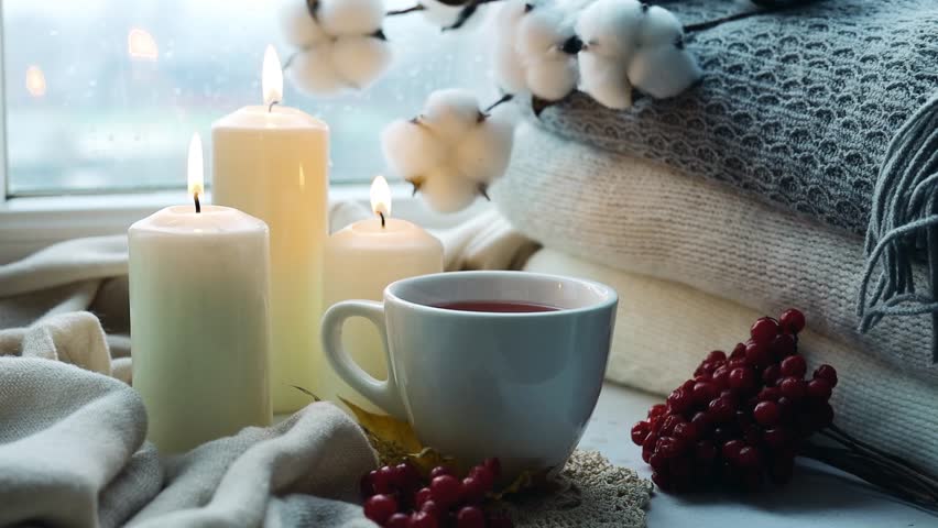 Hello fall, winter.Cozy home mood, rainy weather. Candles,sweaters and tea cup on windowsill.Hot beverage, relaxation, comfort lifestyle.
