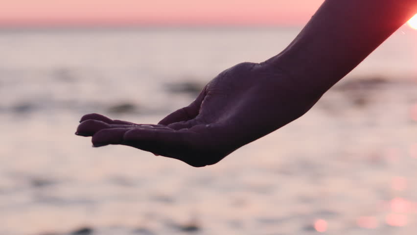 Slow motion handheld closeup young female hand pouring water on her hand on a beach at sunset