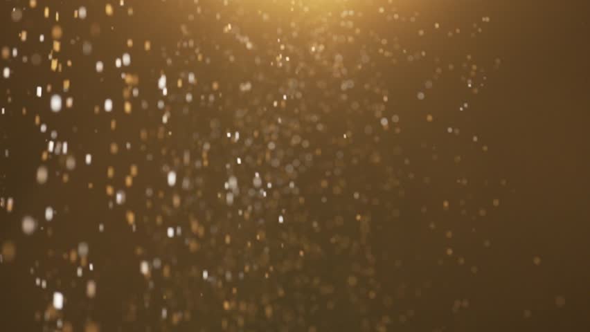 Many sparkling golden glitters floating in warm light on empty background with light from above.