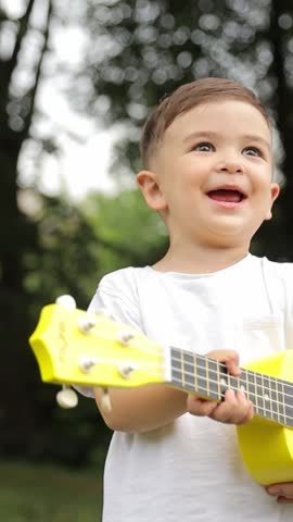 Vertical video a happy little boy playing on the guitar in the park
