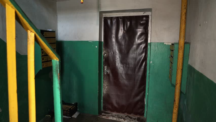 Corridor with old brown entrance doors with leatherette surface. Mailboxes and green walls with rusty yellow sewer pipe. Elements of Soviet interior design in the entrances of houses.
