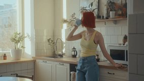 Young girl with red hair standing in modern kitchen filled with daylight, drinking coffee from mug and looking through window during sunny morning at home - Powered by Shutterstock - Get 15% off with code: PIKWIZARD15