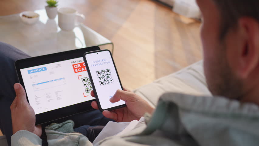 Man scanning invoice qr code and paying with smartphone, over shoulder view. Person using mobile phone and digital tablet for contactless payment at home - Powered by Shutterstock - Get 15% off with code: PIKWIZARD15