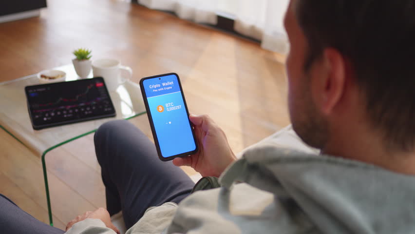 Man confirming cryptocurrency payment with biometric fingerprint scanner on mobile phone, over shoulder view. Using smartphone for crypto wallet payment verification