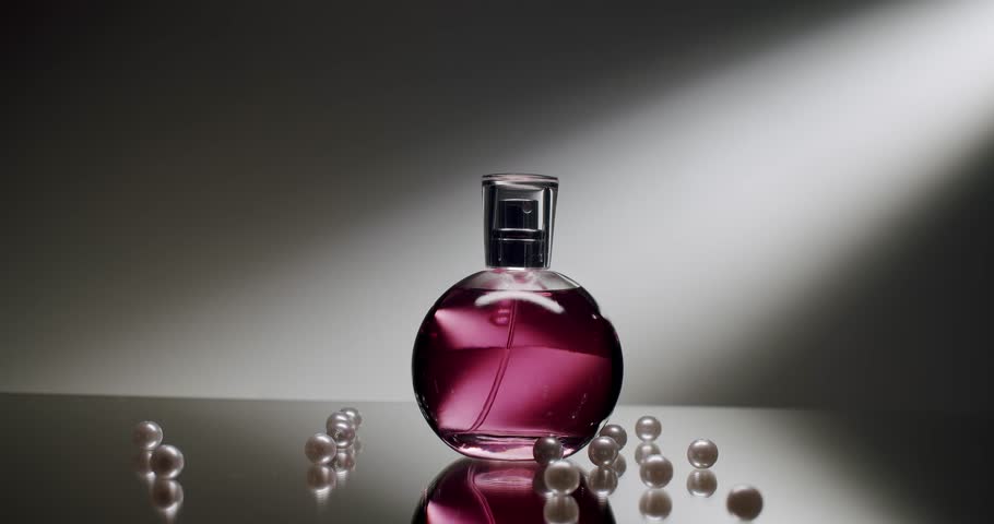 Stylish perfume bottle with pink liquid surrounded by scattered pearls on a reflective surface. Mood lighting highlights the elegance and sophistication of the setting.