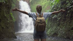 Female tourist with backpack is enjoying view of awesome waterfall among a tropical forest. Woman is opening her arms. Freedom concept. Fairy landscape. Amazing Asian trip. Solo traveler. - Powered by Shutterstock - Get 15% off with code: PIKWIZARD15