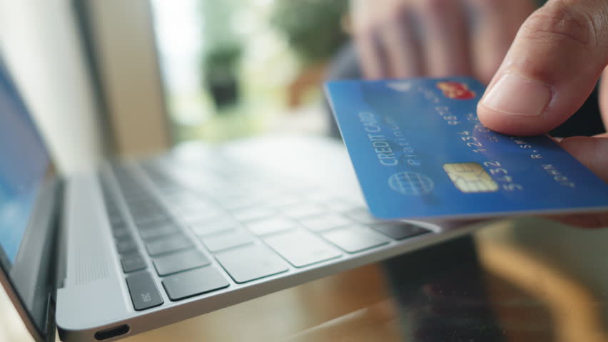 Male hand holding credit card and typing on laptop, paying online closeup. Entering payment details for safe and secure internet shopping