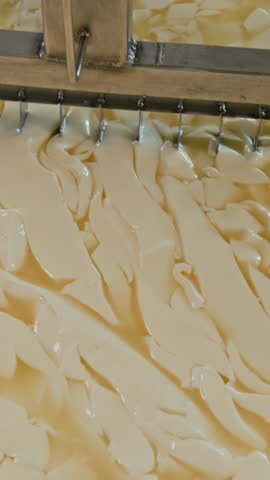 Vertical no people top view of automated steel cutters slicing fermented milk in coagulation vat into pieces, while making cheese at artisan factory