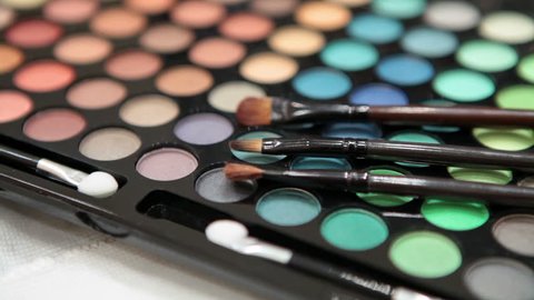 Make-up brushes laying on colorful cosmetic palette. Camera rotation