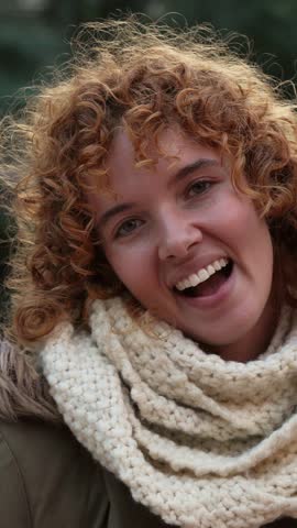 Montage of a young woman with curly red hair and a white scarf smiling in slow motion. Vertical video