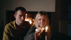 A young couple relaxing by a glowing fireplace as the woman lights candles on the table, setting the mood for a romantic dinner at home. High quality 4k footage - Powered by Shutterstock - Get 15% off with code: PIKWIZARD15