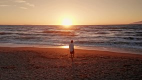 Young man with white shirt walking alone along the beach enjoying the beautiful sunset. waves coming to the shore. Sun is setting. Warm dusk sky. Golden hour. Summer holidays vibes. - Powered by Shutterstock - Get 15% off with code: PIKWIZARD15