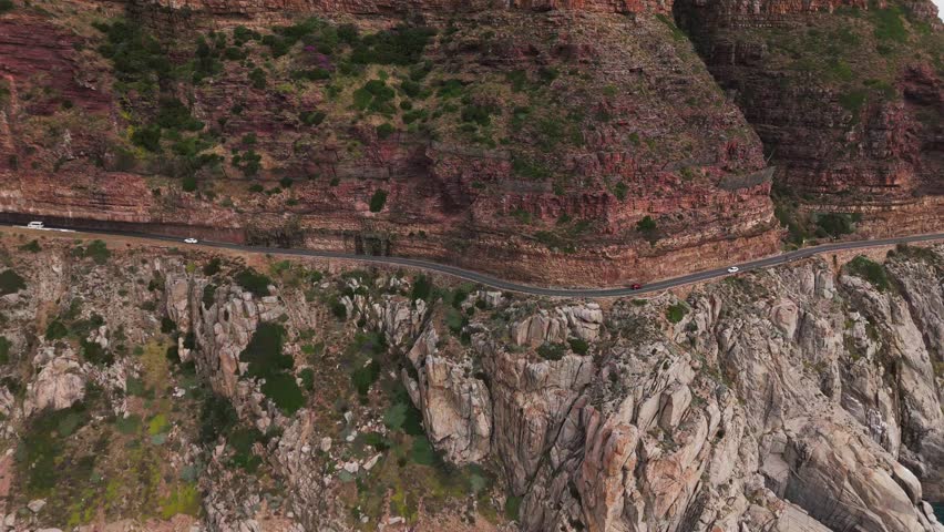 Drone clip of a narrow busy road curving around the outline of a beautiful mountain which highlights the rocky outcrop slope of the mountain