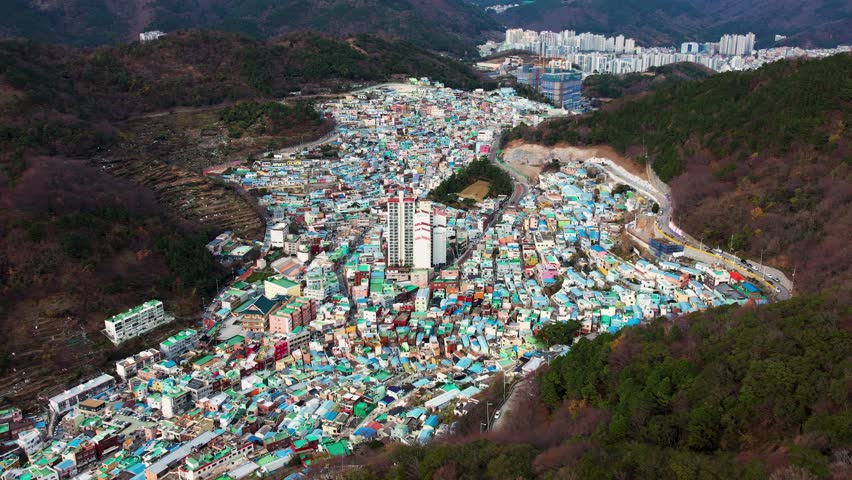 Aerial Drone Footage Captures Gamcheon Village In Busan, South Korea, Showcasing Densely Packed Houses On A Hill, Surrounded By Vibrant Green Forests On A Cloudy Autumn Day, Evoking A Serene Mood.