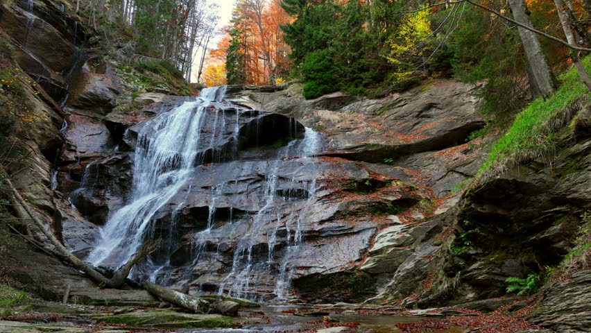 Natural autumn scenery featuring a waterfall, silky water stream over rocks, golden leaves, and the serene beauty of a tranquil forest