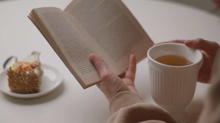Hand Holding Book Over Table with Tea and Pie