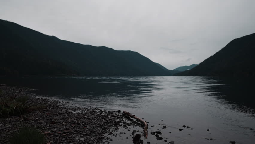 Views of Lake Crescent on a cloudy autumn day. Gentle waves ripple under moody skies, framed by mountains and vibrant fall trees.