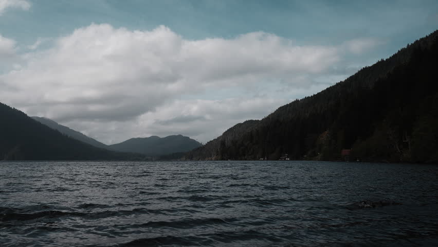 Views of Lake Crescent on a cloudy autumn day. Gentle waves ripple under moody skies, framed by mountains and vibrant fall trees.