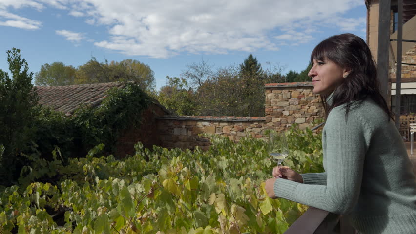 Woman drinking white wine in front of a vineyard