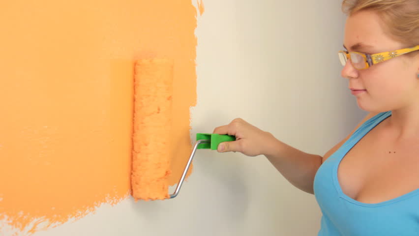 Young girl gaily painting the walls in orange with a paint roller