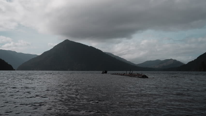 views of Lake Crescent on a cloudy autumn day. Gentle waves ripple under moody skies, framed by mountains and vibrant fall trees.