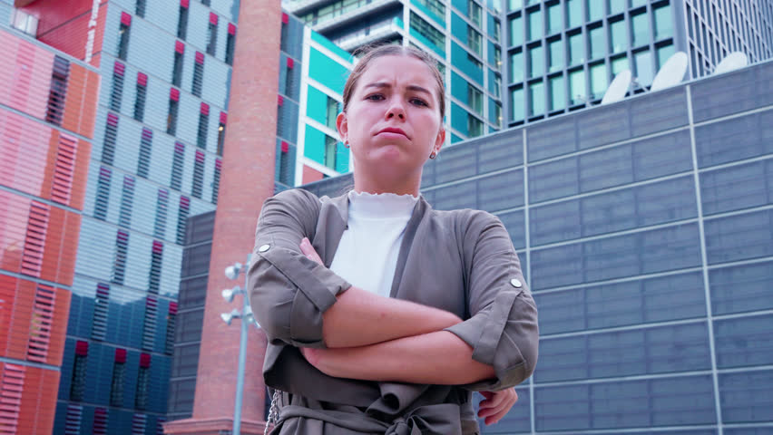 Confident young woman standing in front of urban cityscape with arms crossed.