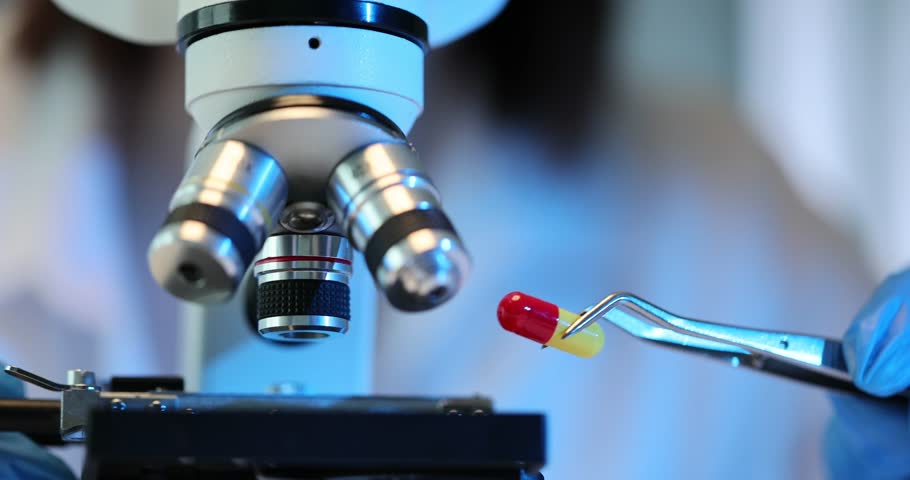 Pharmacist scientist with capsule with medicine under microscope to analyze quality of medicines. Microscopic examination of pharmaceutical compounds in laboratory