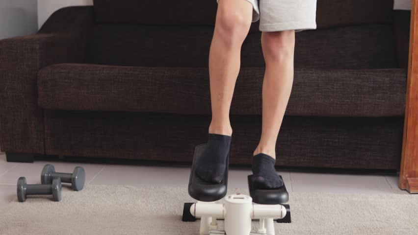 Boy exercising indoors on a mini stepper, focusing on fitness and training. Dumbbells rest on the floor nearby, enhancing the home workout environment