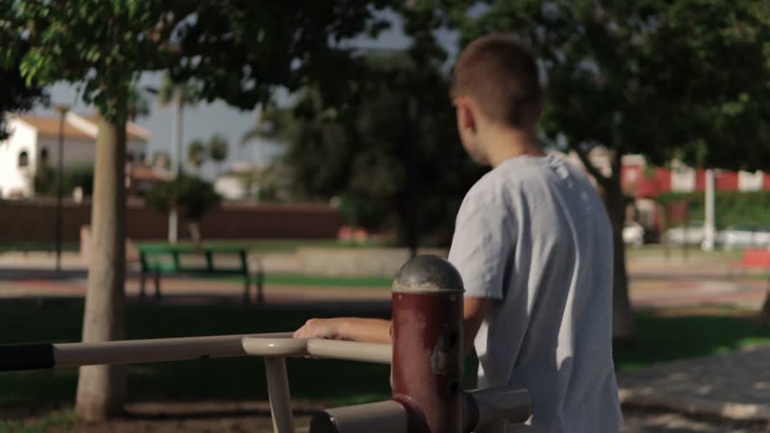 Young boy is working out on outdoor exercise equipment in a park. He is pushing the handles back and forth in a repetitive motion