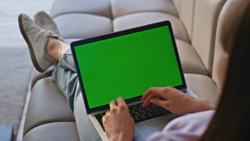 Freelancer typing mockup laptop working online in living room sofa closeup. Unknown woman texting email at green screen computer lying at home couch. Young girl using chroma key device in apartment