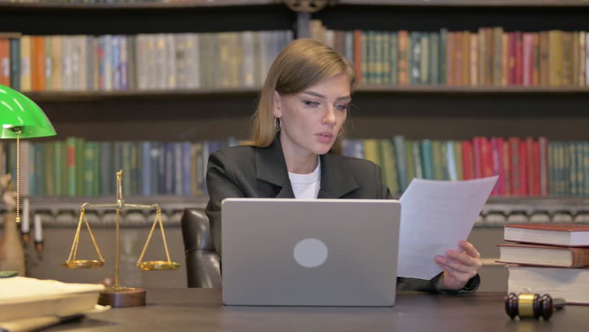 Cheering Female Lawyer Doing Paperwork on Laptop in Office