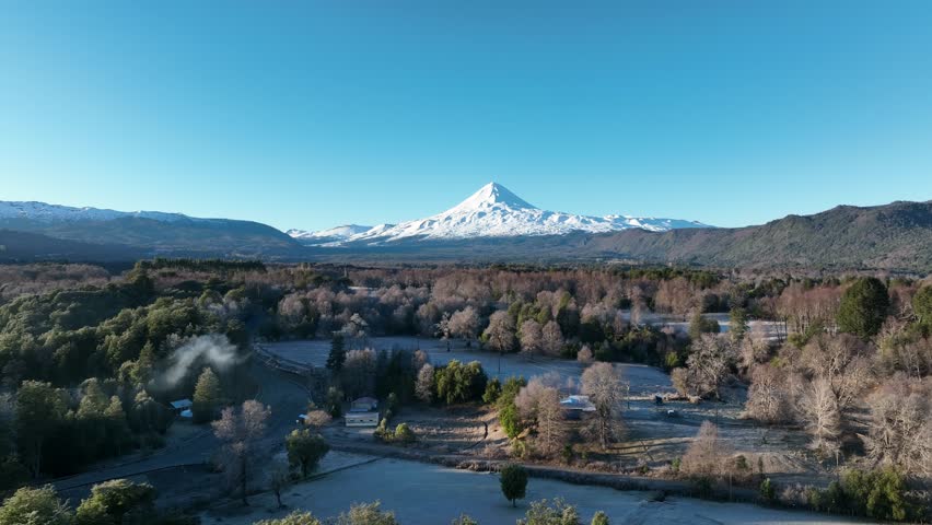 Snow-capped volcano Llaima and forested plains in clear sunlight