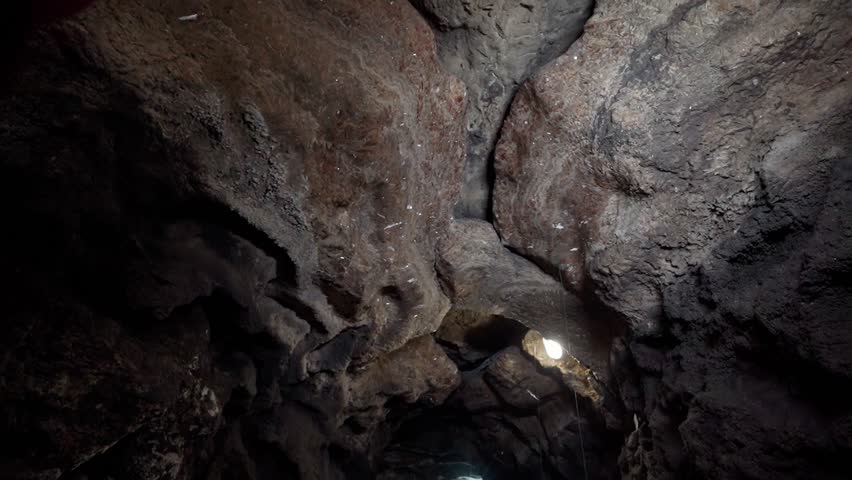 Male explorer walking through a large stone underground cave.