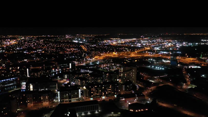 Night time aerial footage of the town of Leeds City Centre taken at night with a drone showing the West Yorkshire city centre all lit up with lights from roads and apartments near the Train Station