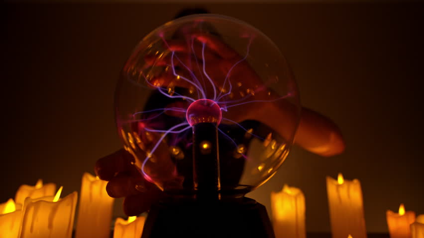 Shooting from below of unrecognizable witch talking with spirits and afterlife. Glowing plasma ball held by fortune teller in candlelit divination session, creating mysterious atmosphere, slow motion.