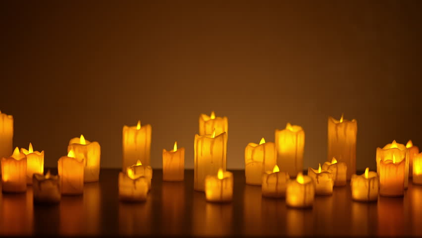 Many lit candles of varying sizes cast warm, inviting glow in dimly lit room, creating peaceful and atmospheric ambiance. Lot small burning candles in dark room, nobody. Shooting in slow motion.