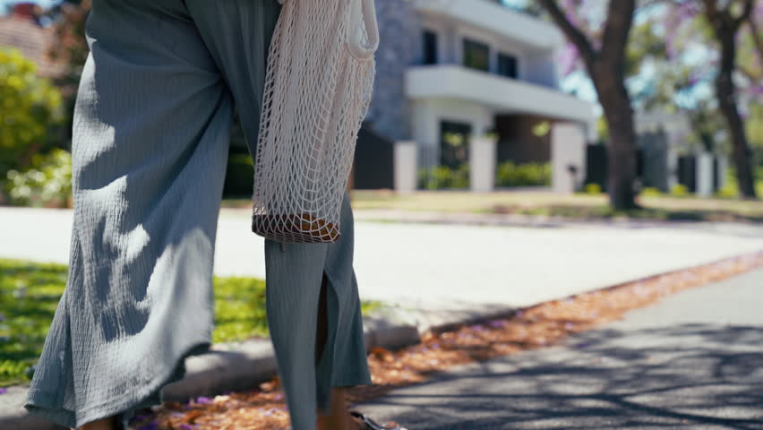 Close-up of a person strolls leisurely along a sunny street carrying an empty mesh bag with a wallet in it