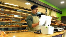Latin friendly salesman in apron using computer stranding in the counter of a bakery shop - Powered by Shutterstock - Get 15% off with code: PIKWIZARD15