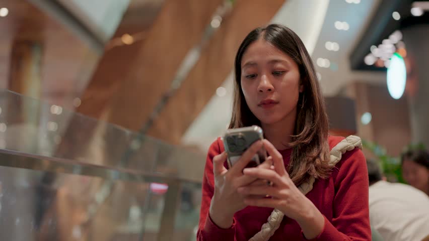 A moment of reflection in a modern shopping mall. A young woman sits still in a chic contemporary shopping mall.