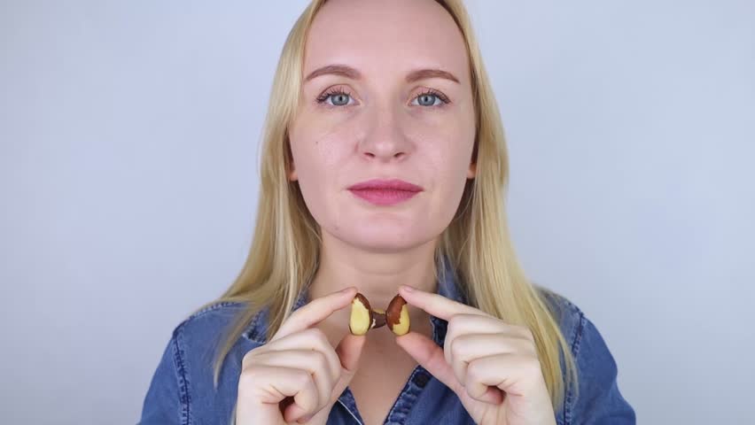 Prevention of thyroid disease. Woman holding a brazil nut in the shape of a thyroid gland. Nut rich in selenium