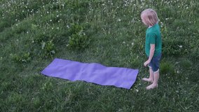 Young person rolling a purple yoga mat in a grassy field, showcasing a serene moment in slow motion - Powered by Shutterstock - Get 15% off with code: PIKWIZARD15