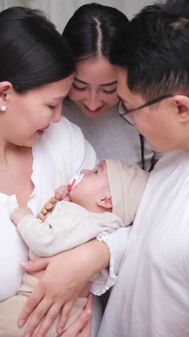 Family embracing cute infant child boy with love in the room. Smiling asian mother, father and aunt holding sleeping newborn baby. Slow-motion