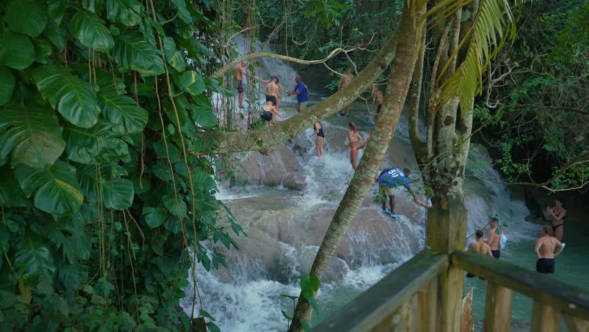 View of waterfall in Dunn’s River Falls and Park Jamaica. Ocho Rios. People are climbing a waterfall over rocks, helping each other along the way.